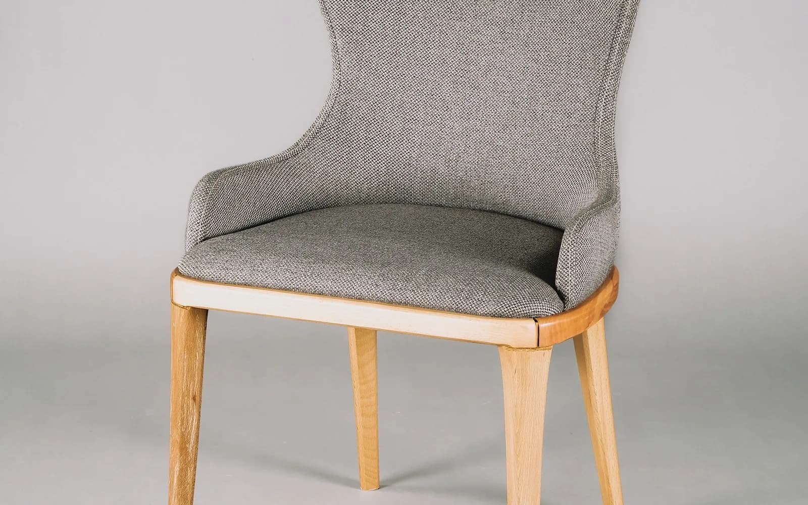 A grey upholstered chair with an oak frame on a pale background
