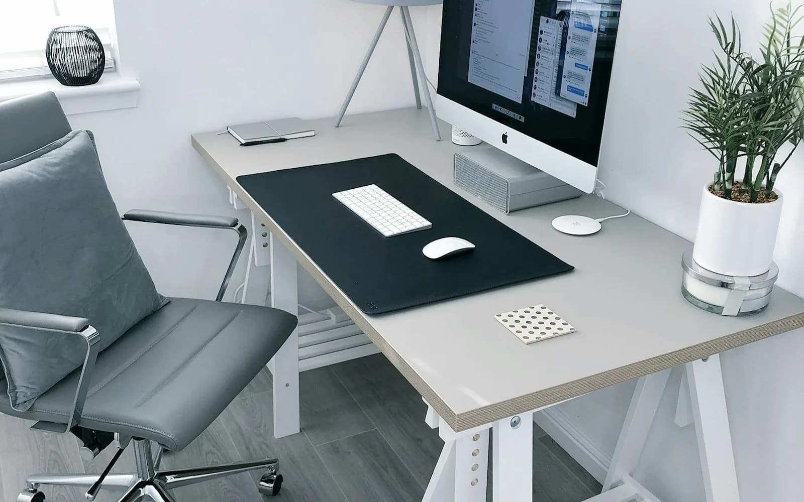 A pale desk with a monitor, lamp and a single plant